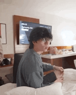 a young man is sitting on a bed in front of a tv .