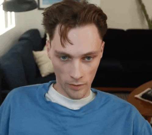 a man in a blue shirt is looking at the camera with a couch in the background