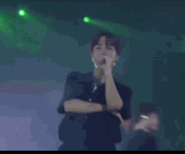 a man is singing into a microphone on a stage with green lights in the background