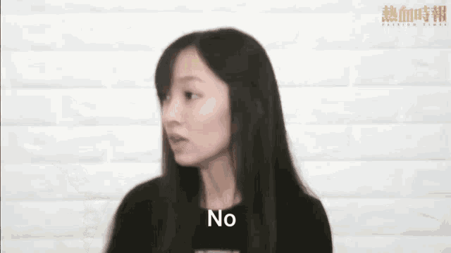 a woman with long hair is standing in front of a white brick wall and saying no .