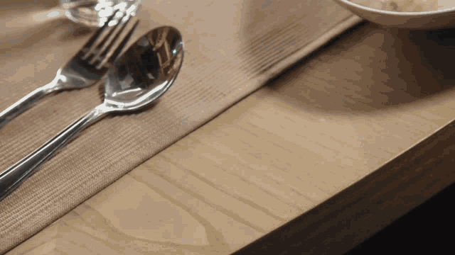 a spoon and fork are on a table with a bowl in the background