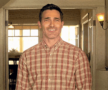 a man in a plaid shirt stands in a doorway smiling