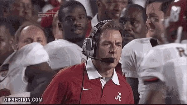 a man wearing headphones and a red shirt with the letter a on it stands in front of a group of football players .