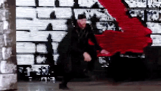 a man in a black jacket is dancing in front of a large screen with the word wwe on it .