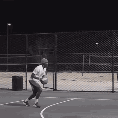 a man is dribbling a basketball on a court with a fence behind him