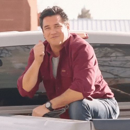 a man in a maroon shirt is sitting in the back of a truck