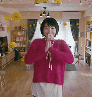 a woman in a pink sweater is standing in a living room with her hands together .