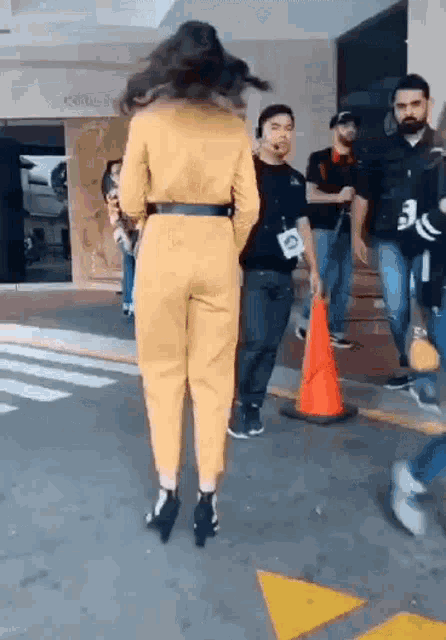 a woman in a yellow jumpsuit is walking down a street next to a man in a black shirt .