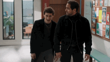 two men are walking down a hallway holding hands and talking .