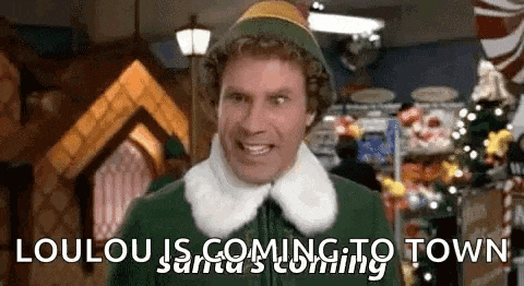 a man in an elf costume is standing in front of a christmas tree in a room .
