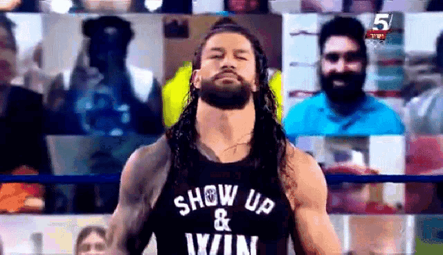 roman reigns is wearing a show up and win shirt while standing in the ring .