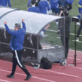 a man in a blue jacket stands on a track with his hands in the air