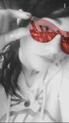 a black and white photo of a woman wearing red sunglasses and a hoodie