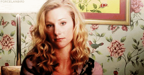 a woman with blonde hair is sitting in front of a floral wallpaper and a lamp .