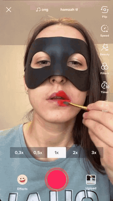 a woman wearing a black mask is applying red lipstick on her lips