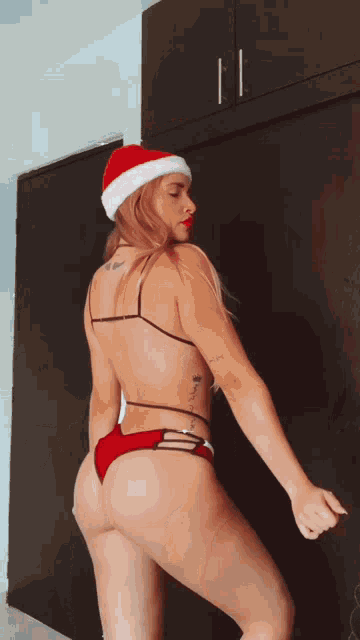 a naked woman in a santa hat is dancing in a room .