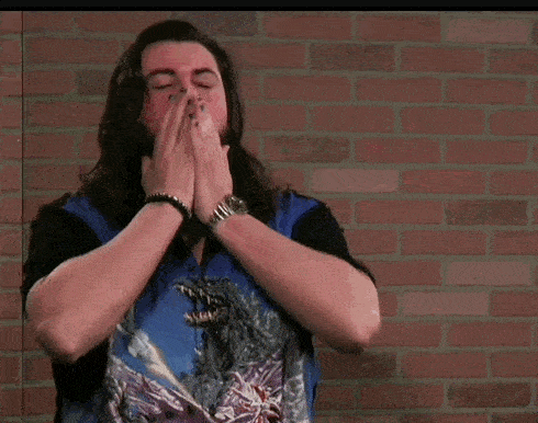 a man with long hair and a beard is standing in front of a brick wall with his hands outstretched .