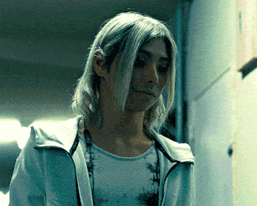 a man with long blonde hair is wearing a white jacket and a t-shirt that says nothing on it