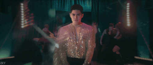 a man in a sequined shirt sings into a microphone with zky written on the bottom