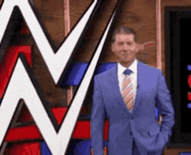 a man in a blue suit and tie is standing in front of a wrestling logo