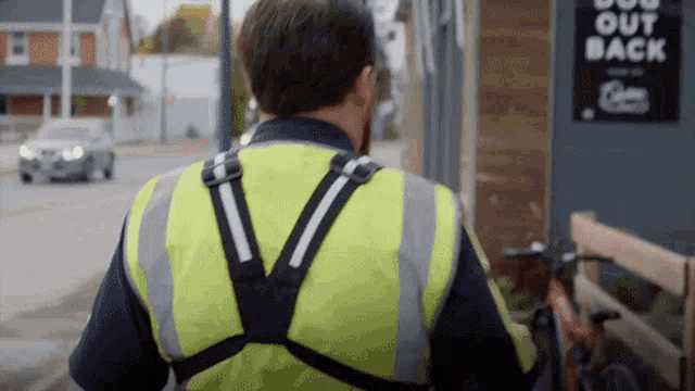 a man wearing a yellow vest is walking down the street with a bicycle .