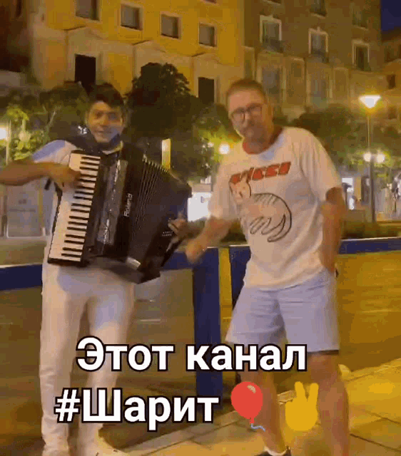 a man is playing an accordion while another man is dancing in front of a yellow building