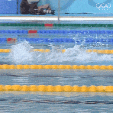 a person is taking a picture of a swimming pool with the olympic rings on the wall