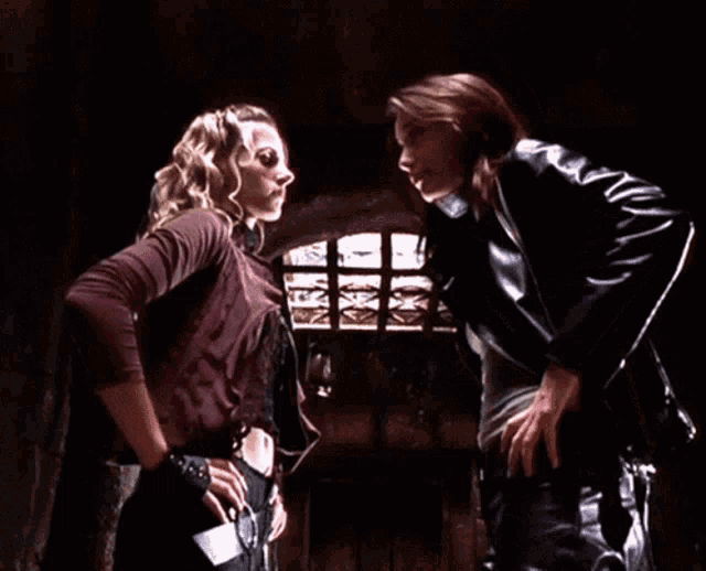 two women standing next to each other in a dark room looking at each other