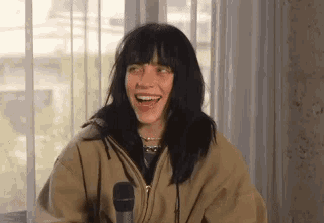 billie eilish is laughing while talking into a microphone .