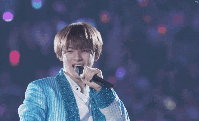 a man in a blue sequined jacket is holding a microphone
