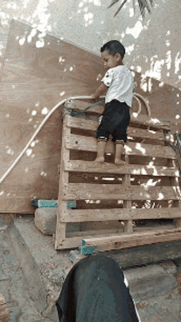 a little boy is standing on a wooden pallet with a hose attached to it