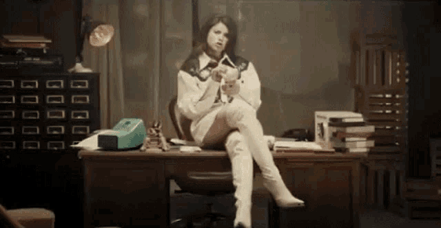 a woman is sitting at a desk with her legs crossed and holding a gun .