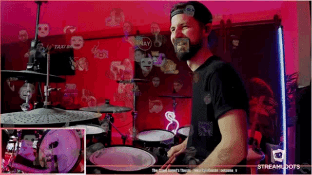 a man is playing drums in front of a red wall that says taxi on it