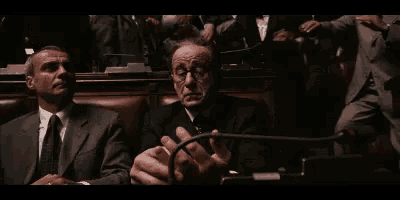 two men in suits and ties are sitting in a row in a dark room .
