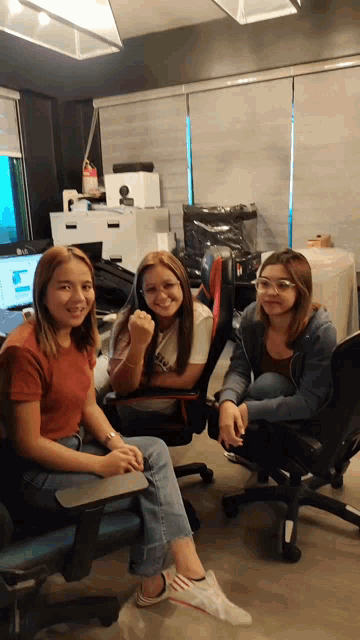 three women are sitting in chairs in an office smiling for the camera