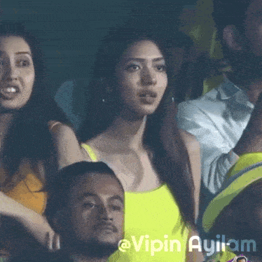 a woman in a yellow tank top sits in a crowd with the name vipin ayilam written on the bottom