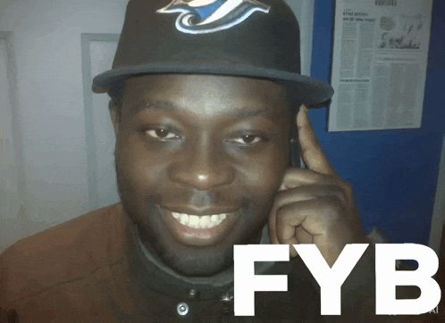 a man wearing a blue jays hat talks on a phone