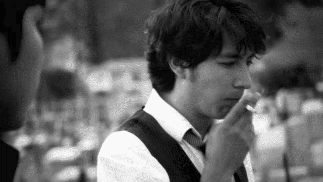 a man in a vest and tie is smoking a cigarette