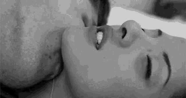 a black and white photo of a man and a woman kissing .