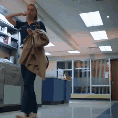 a woman is walking down a hallway in a hospital holding a coat