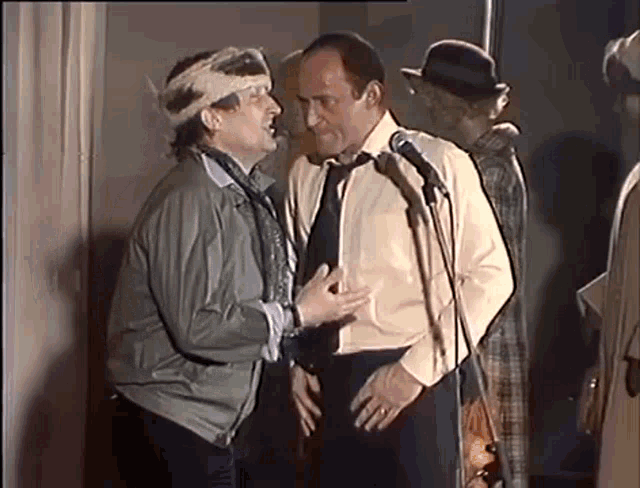 two men are standing next to each other in front of a microphone in a room .