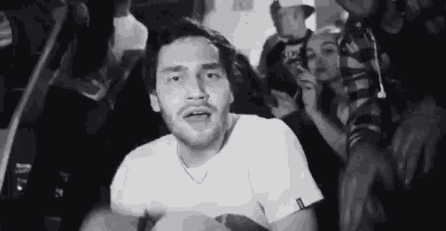 a man in a white t-shirt is surrounded by a crowd of people .