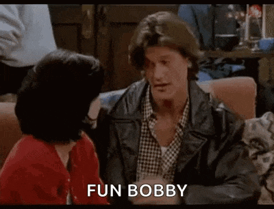a man and a woman are sitting on a couch talking to each other . the man is wearing a leather jacket .