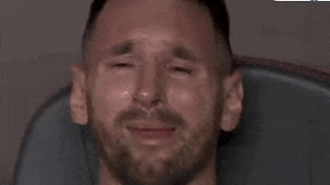 a man with a beard is crying with tears running down his face while sitting in a chair .