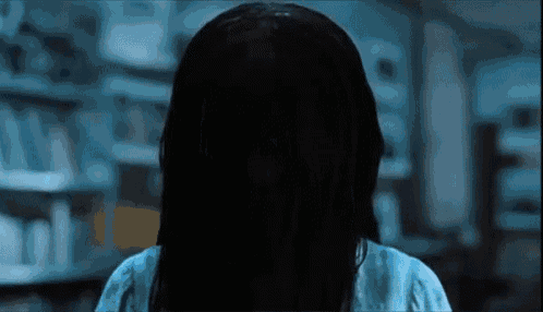 a woman with a ring in her hair is standing in a dark room in front of a bookshelf .