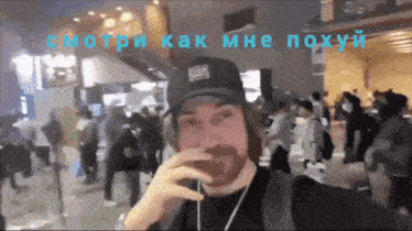 a man with a beard wearing a hat and headphones stands in front of a crowd of people