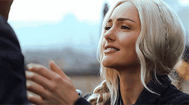 a woman with blonde hair is smiling while holding a man 's hand .