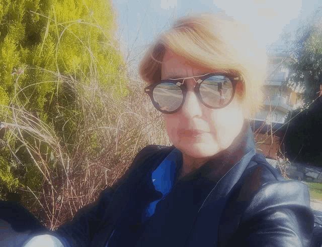a woman wearing sunglasses is taking a selfie in front of a bush