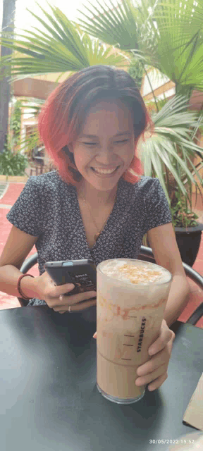 a woman sits at a table with a starbucks drink and a cell phone