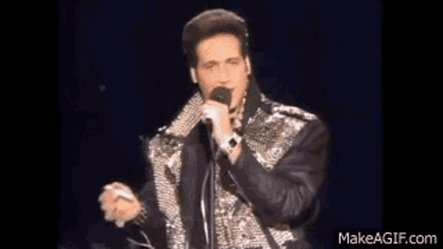 a man is singing into a microphone while wearing a leather jacket .